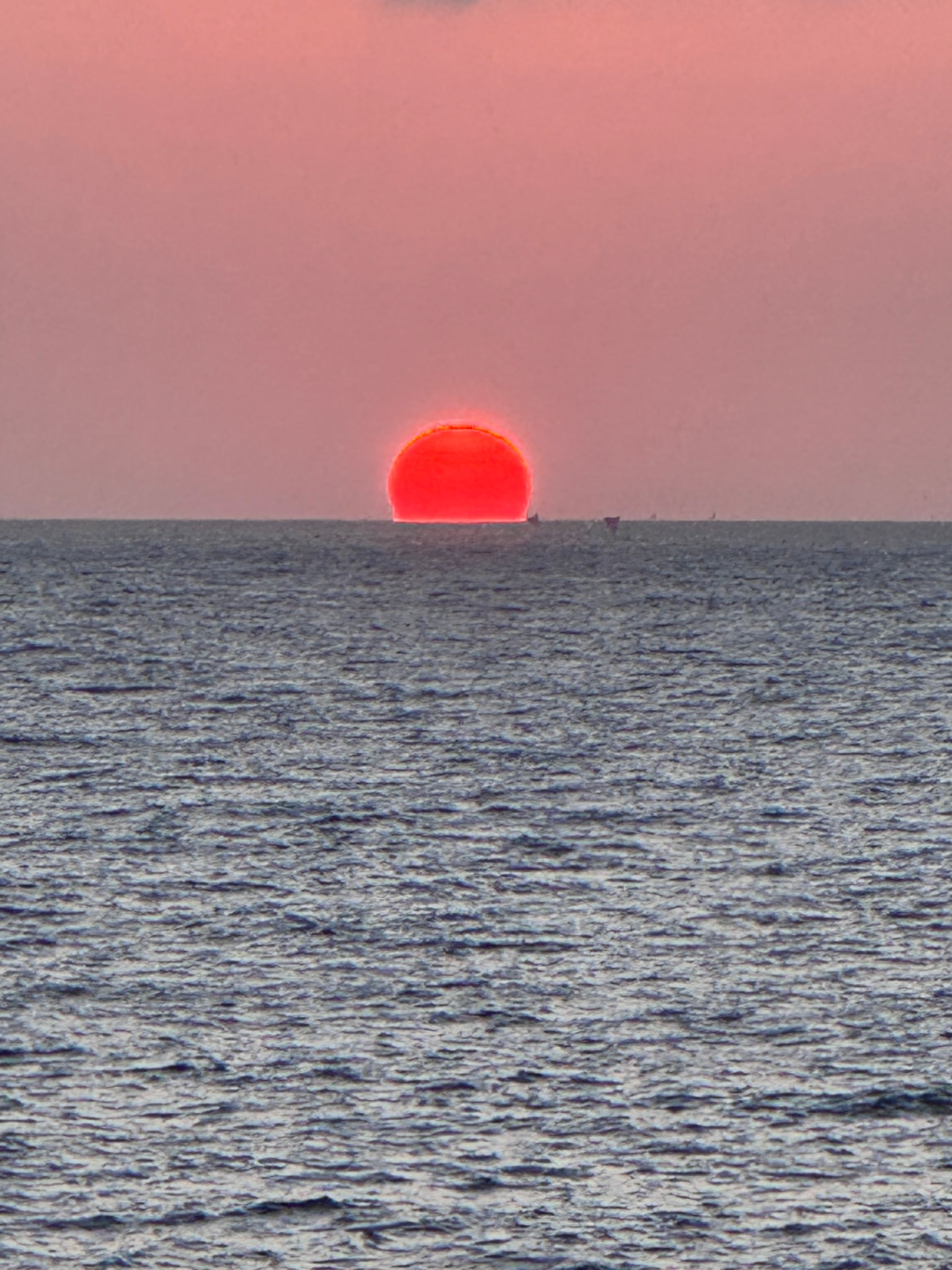 A red sun touching the horizon over a calm sea at dusk