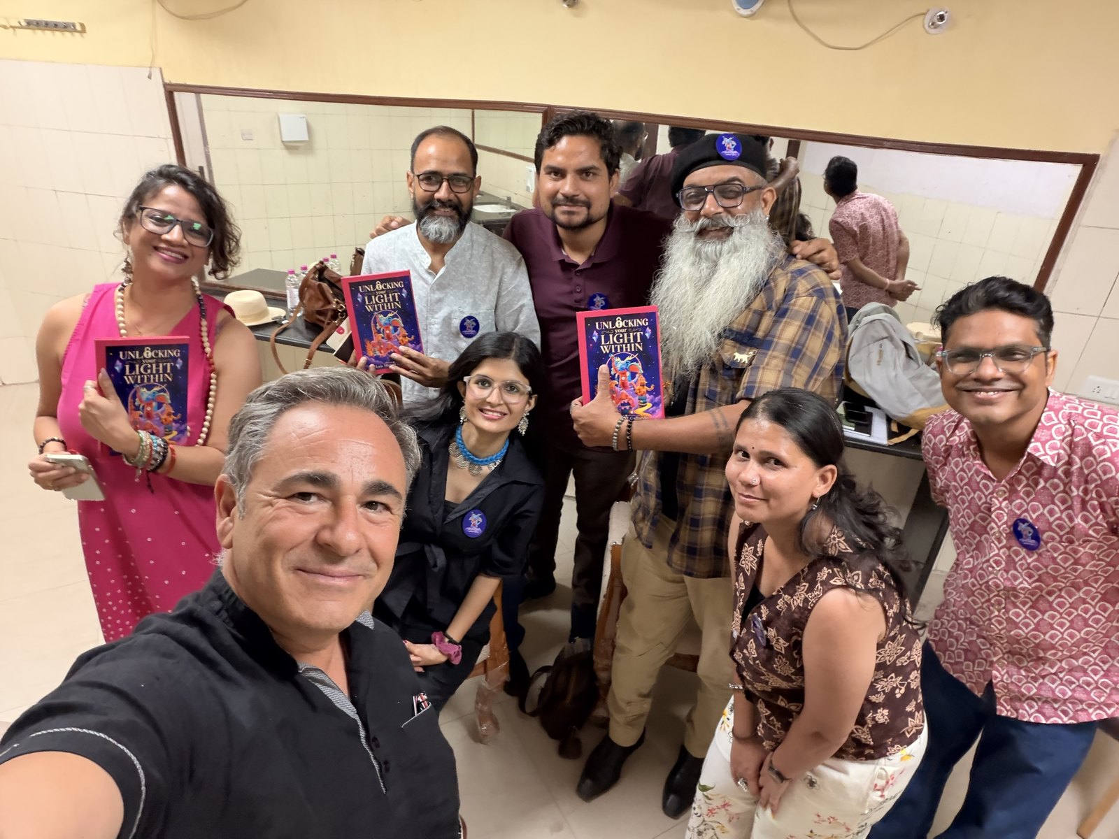 Luis Miguel Gallardo se hace un selfi sonriente con ocho amigos, tres de los cuales sostienen ejemplares del libro Unlocking Your Light Within.